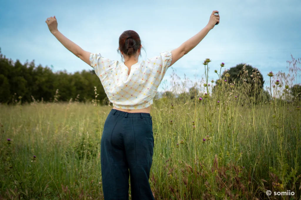 Pantalon Twig Woven Pant en lin marine vu de dos, bras levés dans un champ, avec un top écru à pois colorés