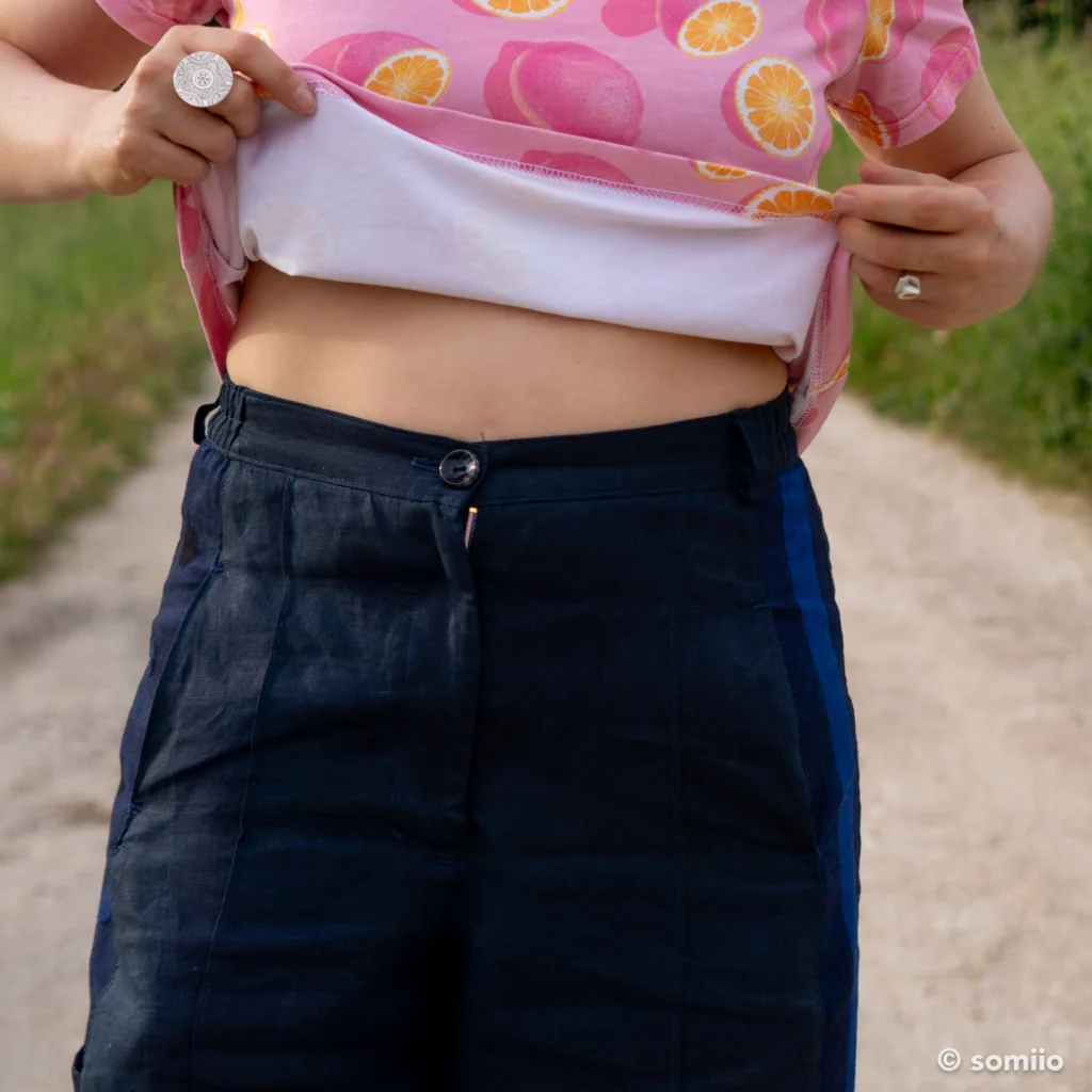 Détail de la braguette boutonnée du pantalon Twig Woven Pant en lin marine, avec le décalage entre bouton et braguette