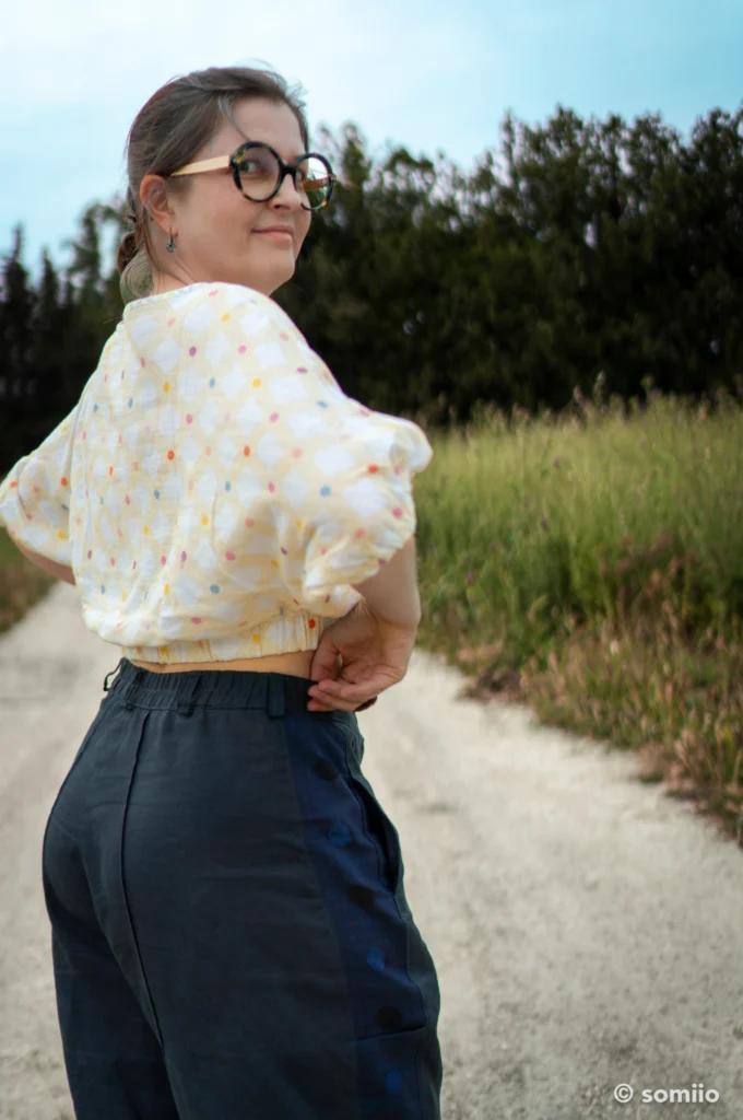 Mains dans les poches prises dans les coutures du pantalon Twig Woven Pant en lin bleu marine, porté avec un top écru à pois colorés