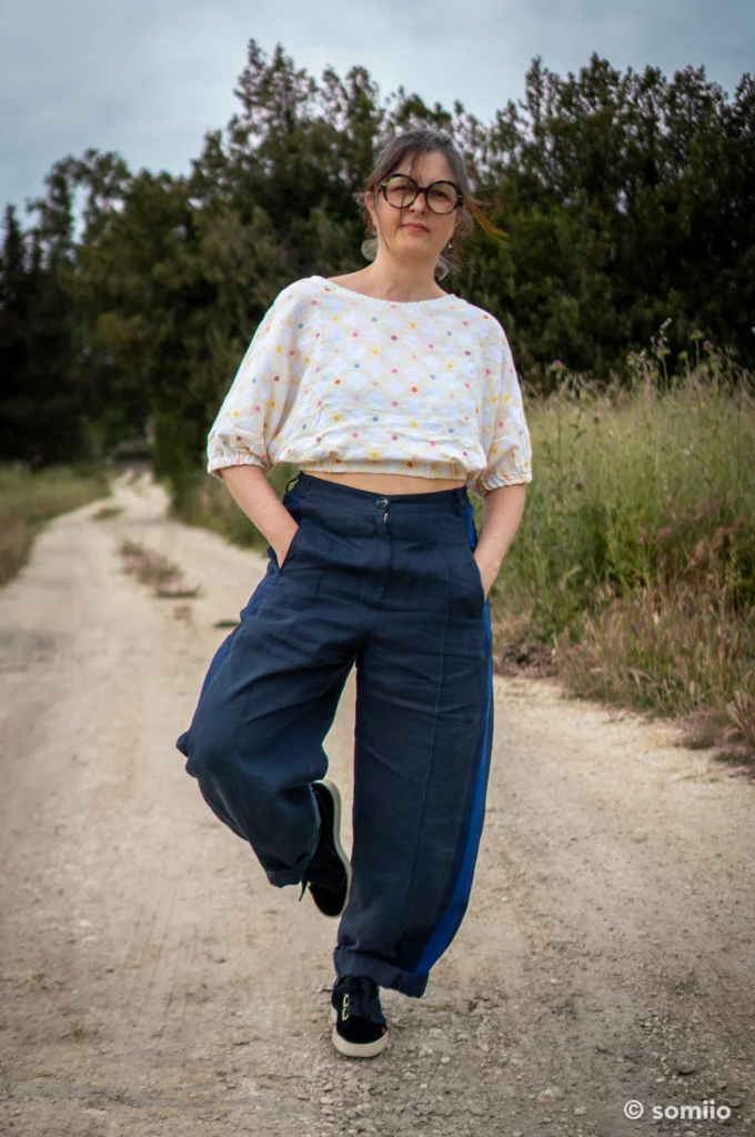 Pantalon Twig Woven Pant de Style Arc cousu en lin bleu marine, forme barrel longueur cheville, porté avec un t-shirt rose à motif agrumes sur un chemin de campagne