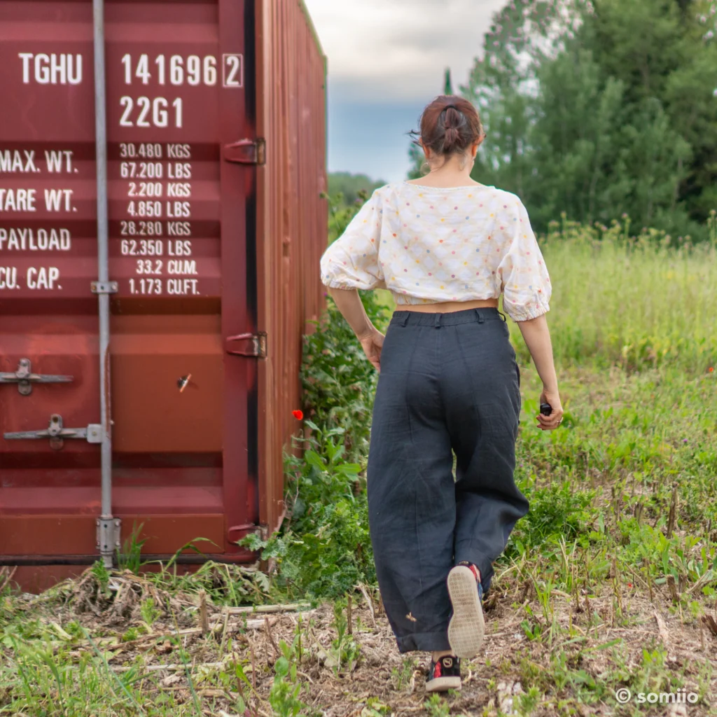 Pantalon barrel Twig Woven Pant en lin marine vu de dos, appuyée contre un container rouge